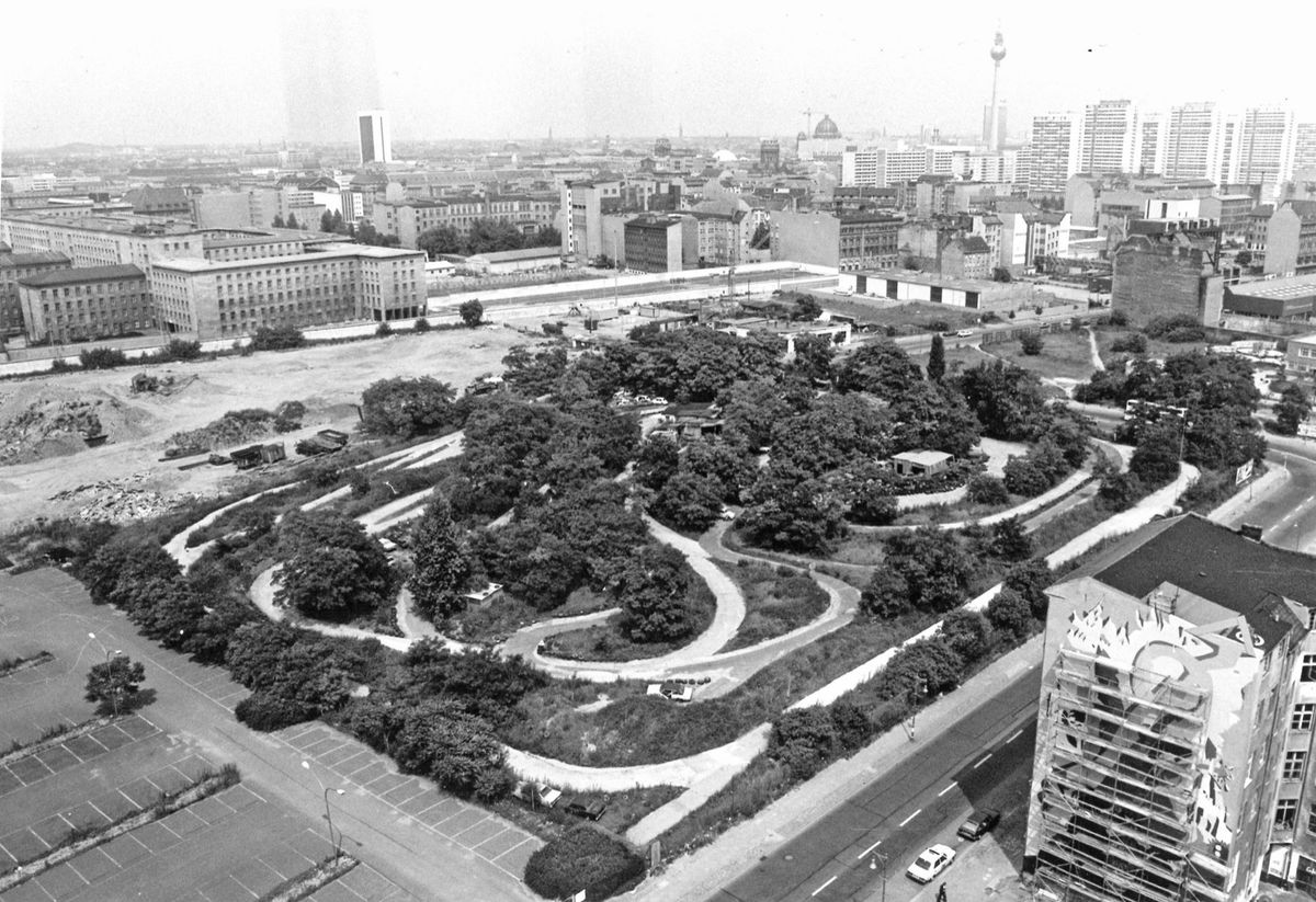 Luftaufnahme eines begrünten Geländes mit stark geschwungenen Wegen, umgeben von städtischer Bebauung und Straßen.